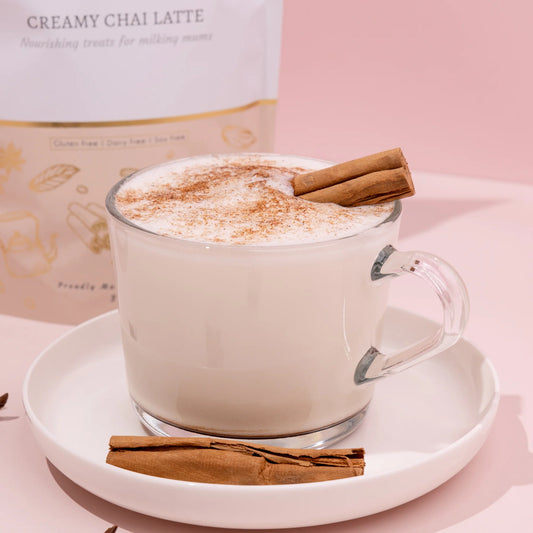 Glass mug of lactation creamy chai latte with cinnamon stick on a pink background made to milk creamy chai latte
