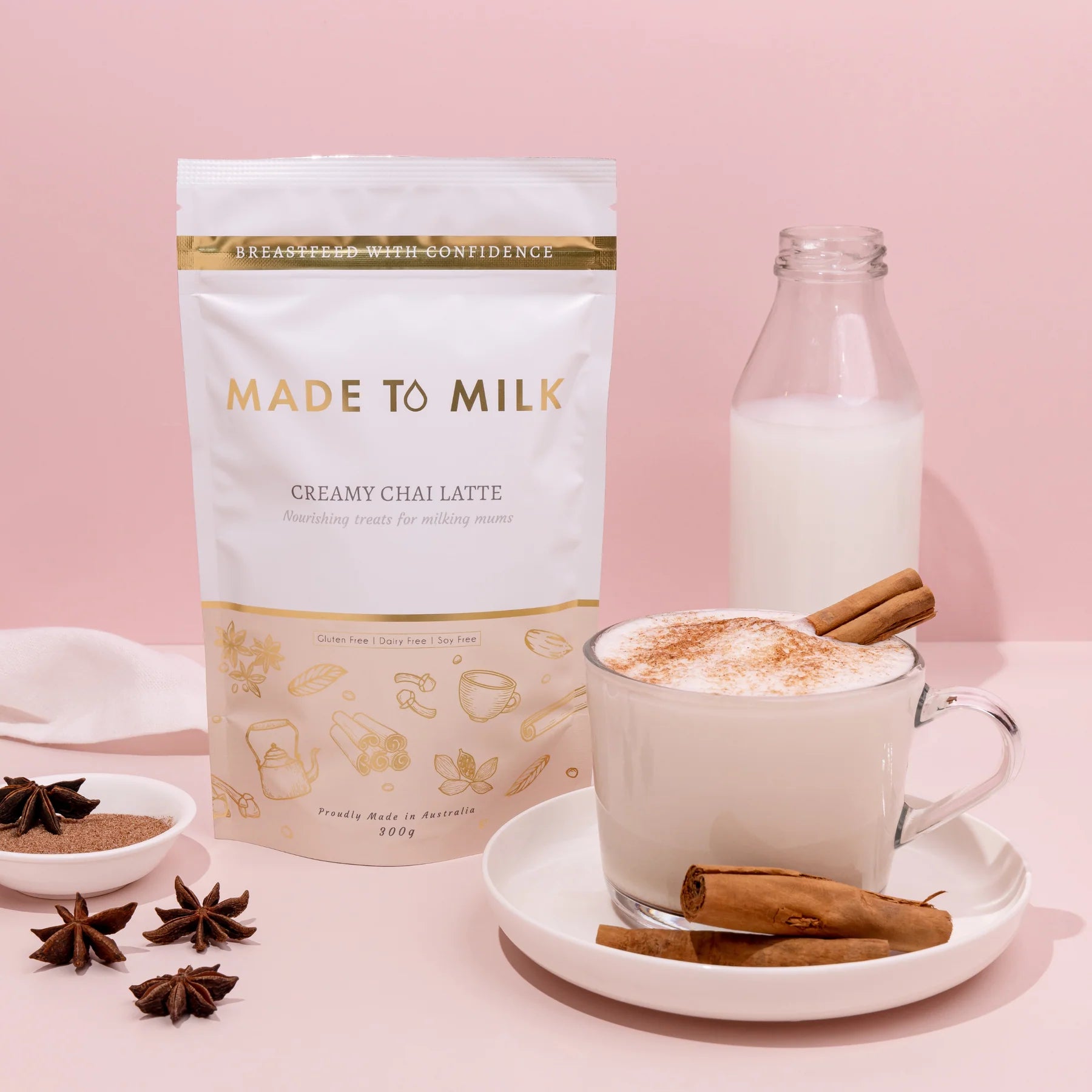Made to Milk lactation creamy chai latte package with a cup of latte, bottle, and spices on a pink background