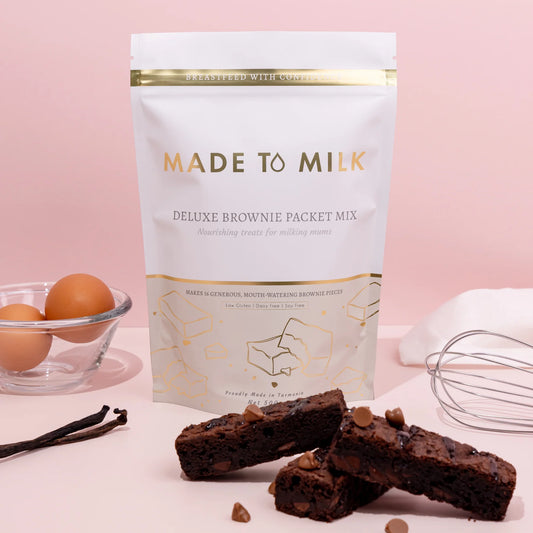 Made to Milk lactation deluxe brownie packet mix with brownies and ingredients on a pink background