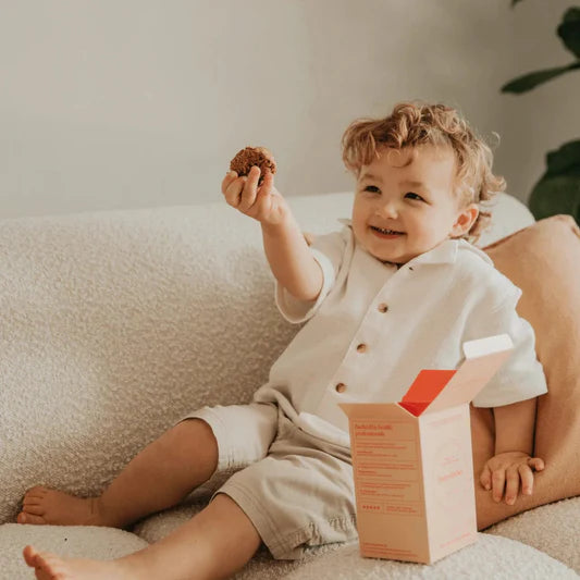 Child sitting on a couch holding a cookie with a box next to them.