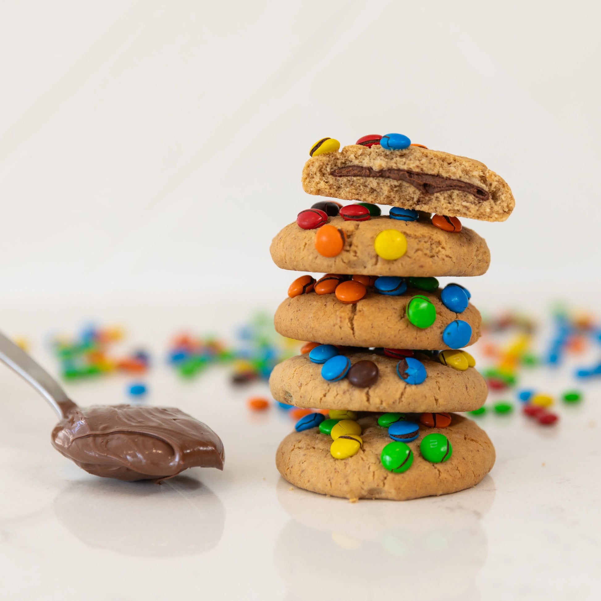 Stack of cookies with mini m&ms and a spoonful of nutella on a light background