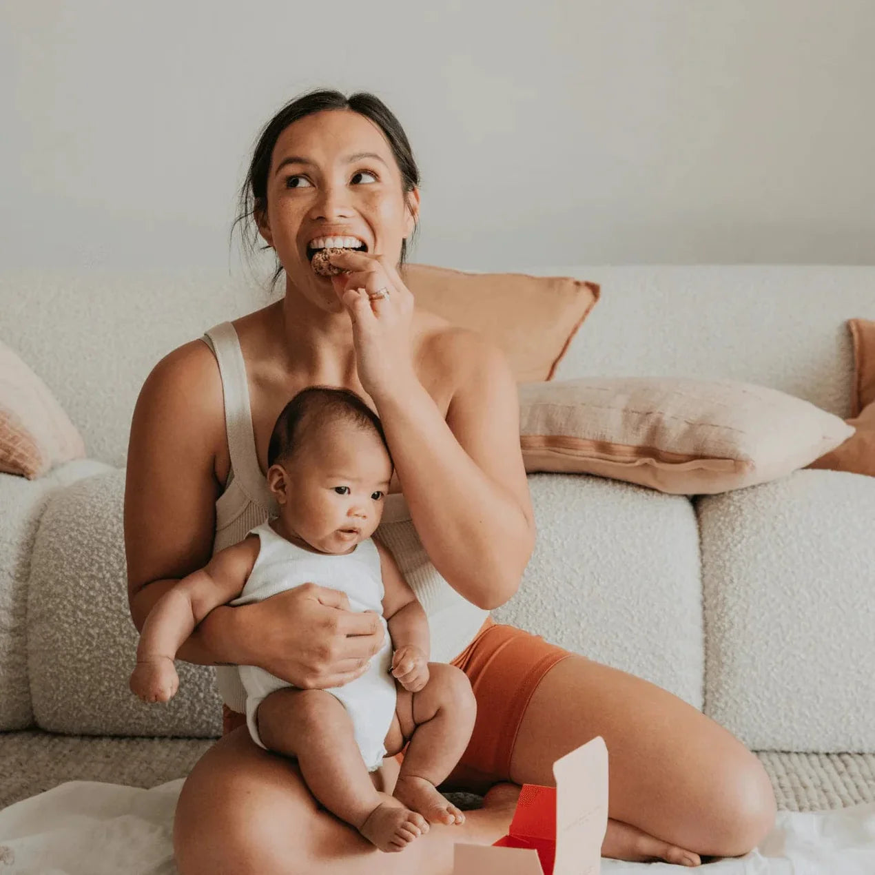 Woman sitting on a couch holding a baby, both looking up with a joyful expression.