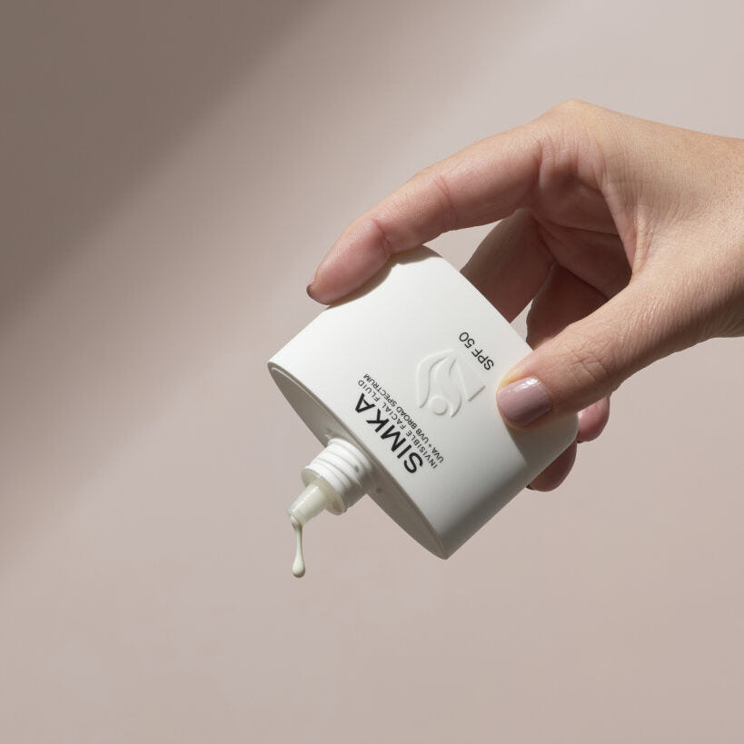 Hand holding a white bottle with a dropper labeled 'SINUKA' against a beige background