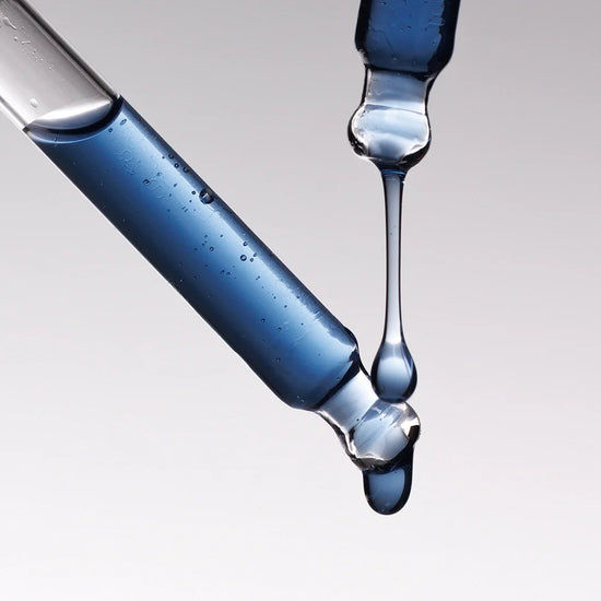 Two droppers with blue liquid being dripped from one onto a gray background