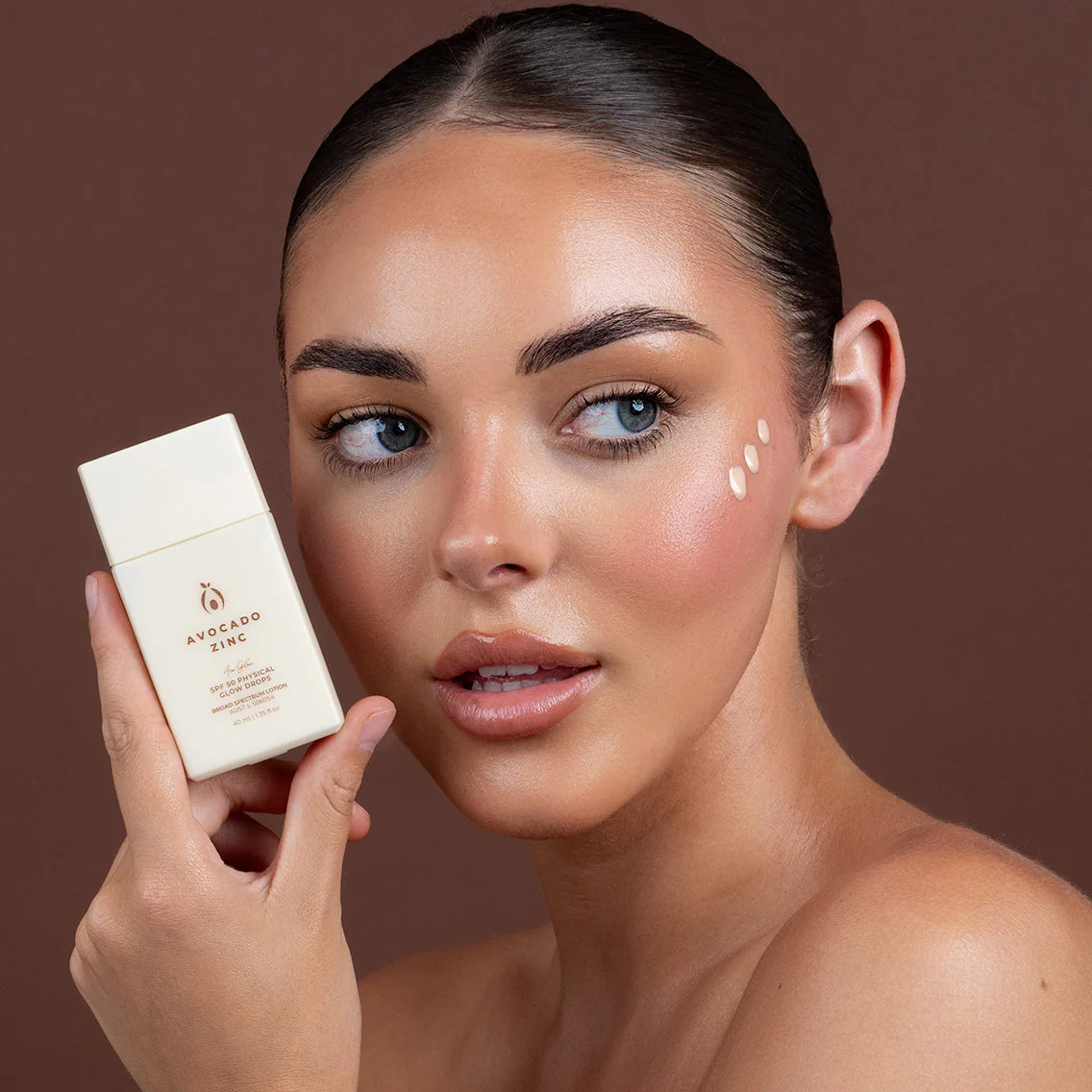 Woman holding a glow skincare product with a brown background