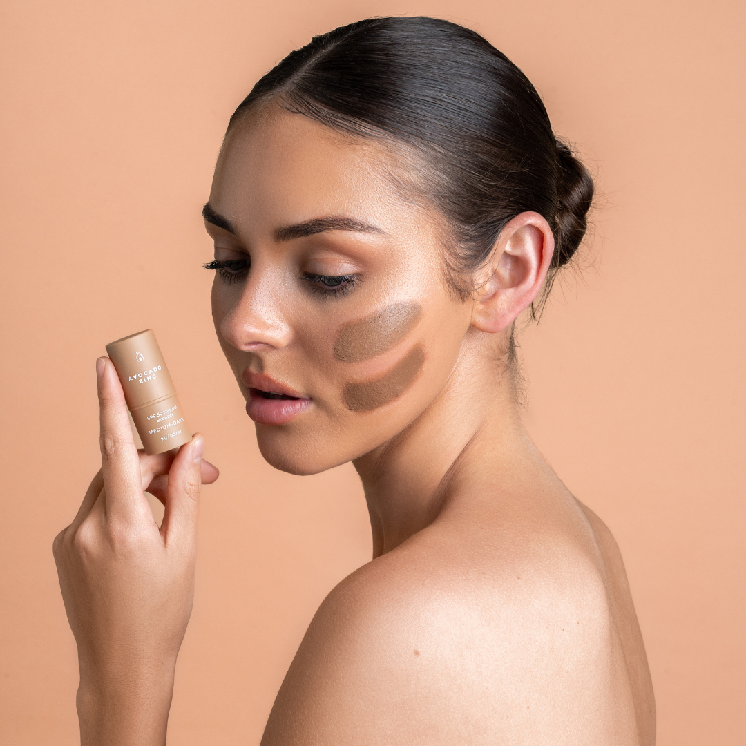 Woman applying makeup with a contour stick on a beige background