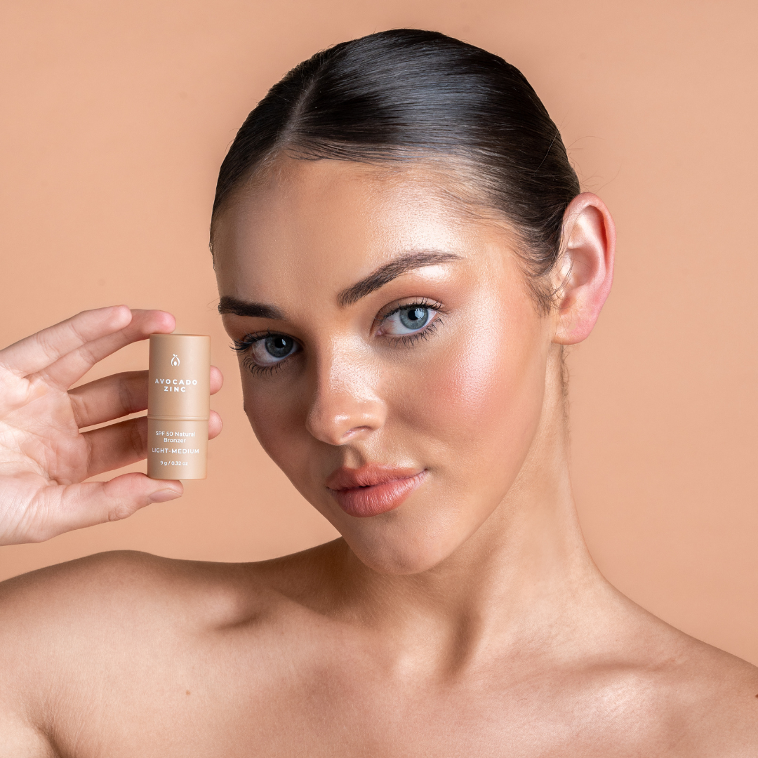 Woman holding a bronzer contour skincare product against a beige background
