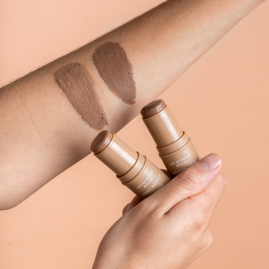 Two contour sticks avozinc with swatches on a person's arm against a beige background