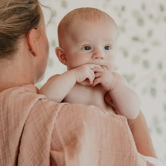 Baby being held by a person with a blurred background with blush pink swaddle