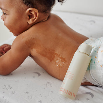 Baby lying on a crib with nappy and a bottle of Bubba's Massage Oil leaning on it with a swatch of oil on it.