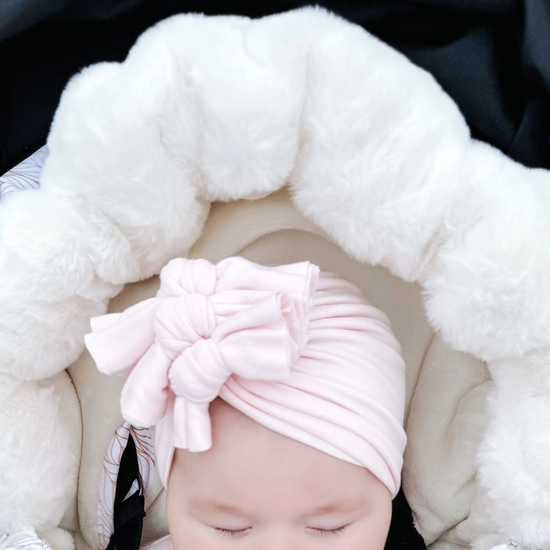 Baby wearing a pink turban with a bow, wrapped in white fluffy baby luno