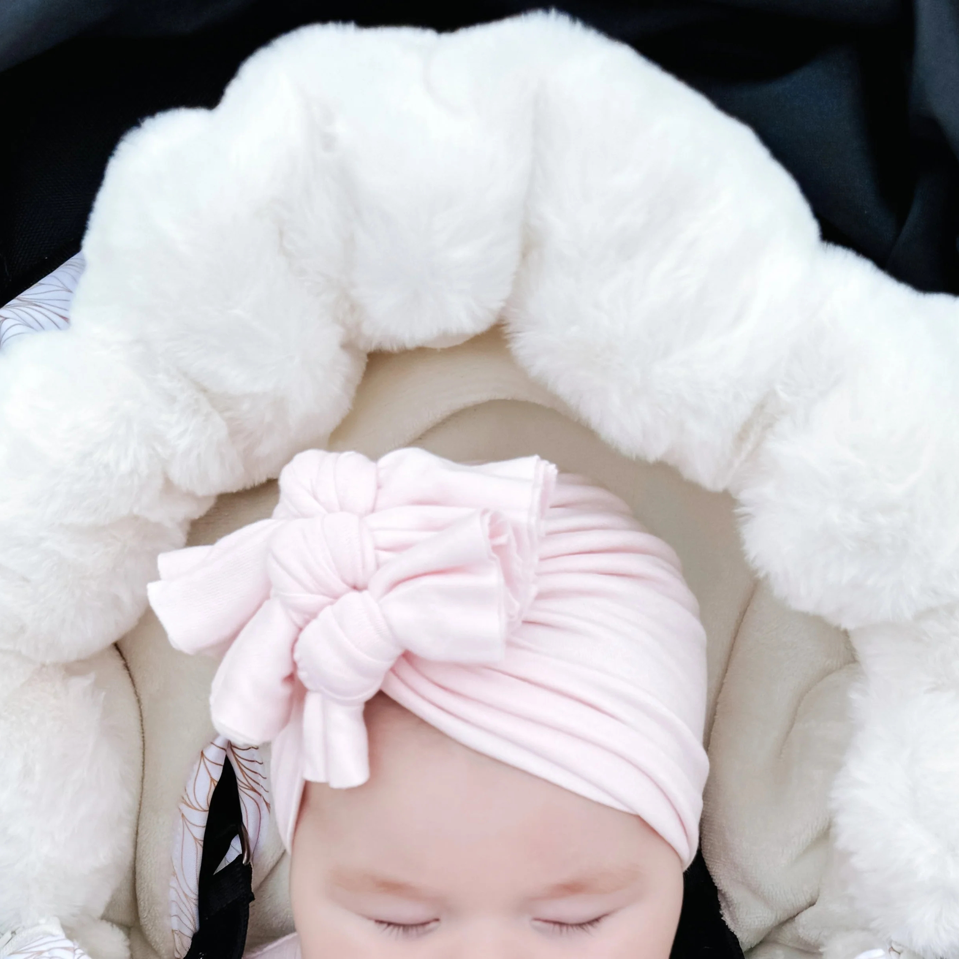 Baby wearing a pink turban with a bow, wrapped in white fluffy baby luno