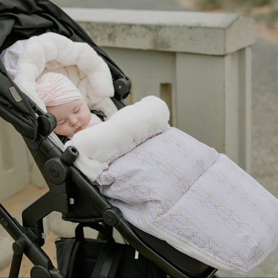 Baby sleeping in a stroller with a white and gold baby luno pram cover and pink hat.