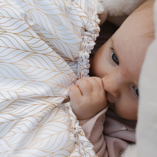 Baby peeking out from behind a textured fabric with gold leaf patterns