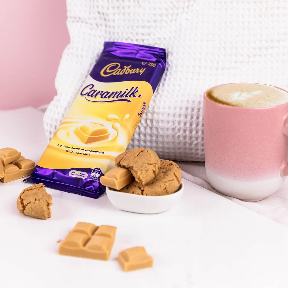 Cadbury Caramilk chocolate bars and cookies with a pink mug on a white surface
