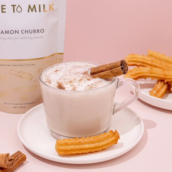 Cup of frothy beverage with cinnamon stick and churros on a pink background