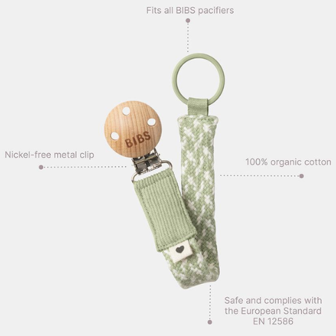 Dummy clip or Pacifier clip. Light timber badge that says bibs on top of metal clip attached. Braided cotton band in green and white with dummy ring on end. Says Fits all bibs pacifiers, 10% organic cotton, Nickel-free metal clip and safe and complies with European standards EN 12586.
