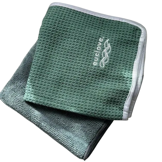 Two folded textured microfiber cloths in green tones, with one placed on top of the other. The top cloth is a medium sage green with a white embroidered 'euclove' logo, and the bottom cloth is a darker gray-green.