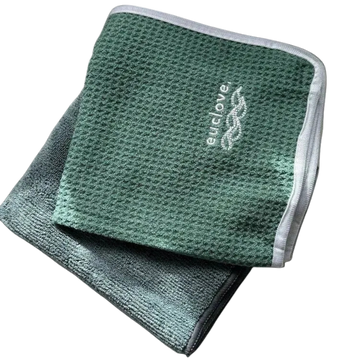 Two folded textured microfiber cloths in green tones, with one placed on top of the other. The top cloth is a medium sage green with a white embroidered 'euclove' logo, and the bottom cloth is a darker gray-green.