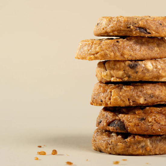 A stack of five thick, textured chocolate chip cookies on a warm beige background. Triple Choco Mama Biscuits franjos