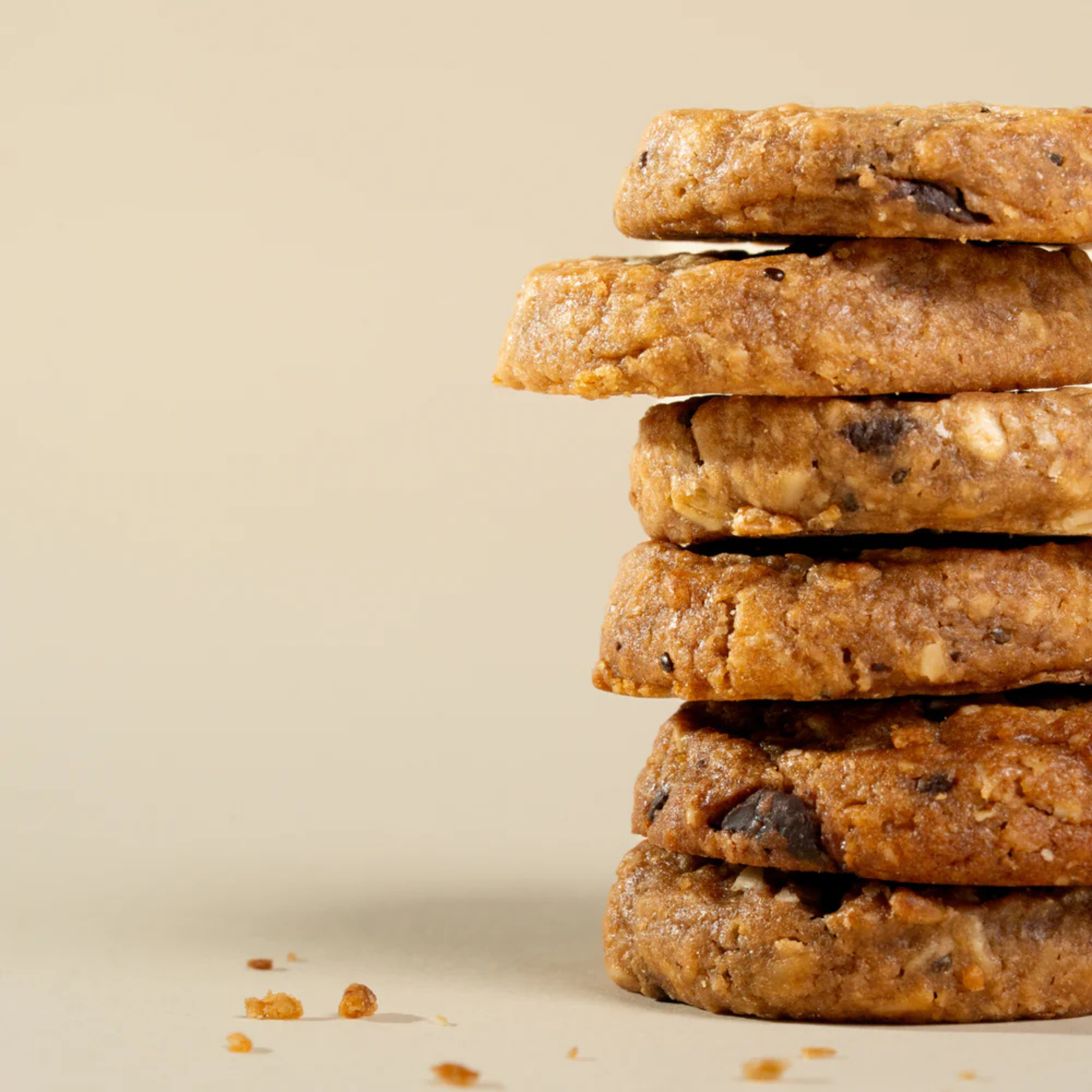 A stack of five thick, textured chocolate chip cookies on a warm beige background. Triple Choco Mama Biscuits franjos