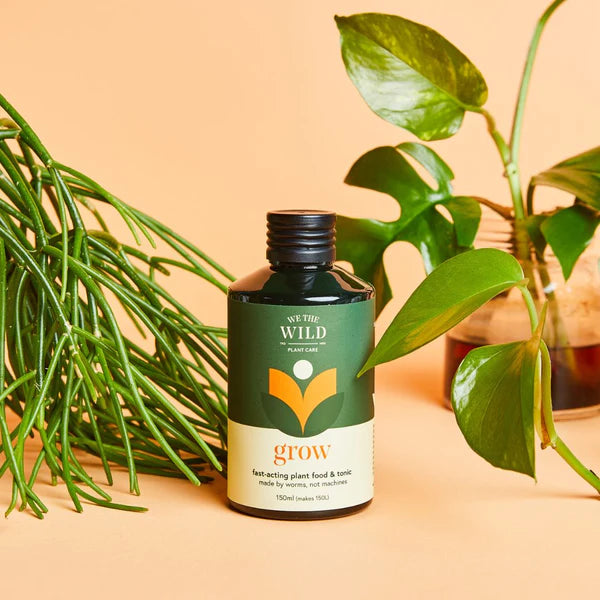 Bottle of 'We The Wild' Grow Concentrate Organic Liquid Plant Food with plants on a beige background