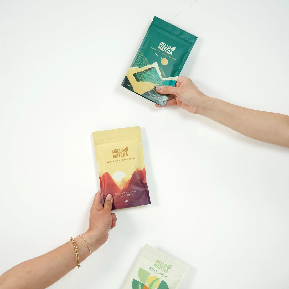 Two hands holding 'Hello Matcha' tea packages against a white background
