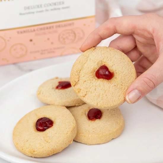 Hand picking a made to milk cookie with jam from a plate with a box in the background