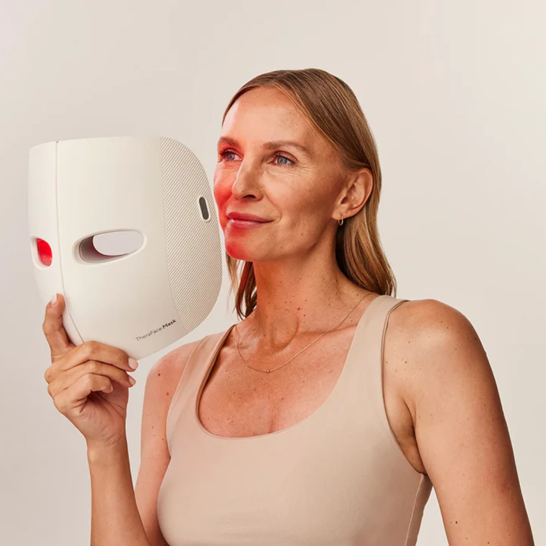 Woman holding a white LED face mask with visible red light on a plain background