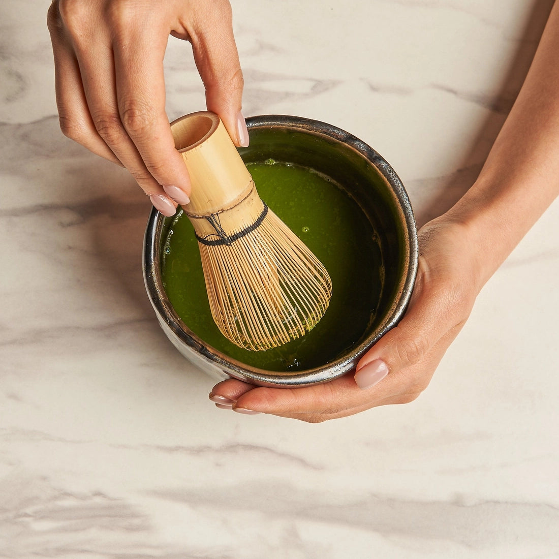 Person preparing matcha green tea with a whisk on a marble surface