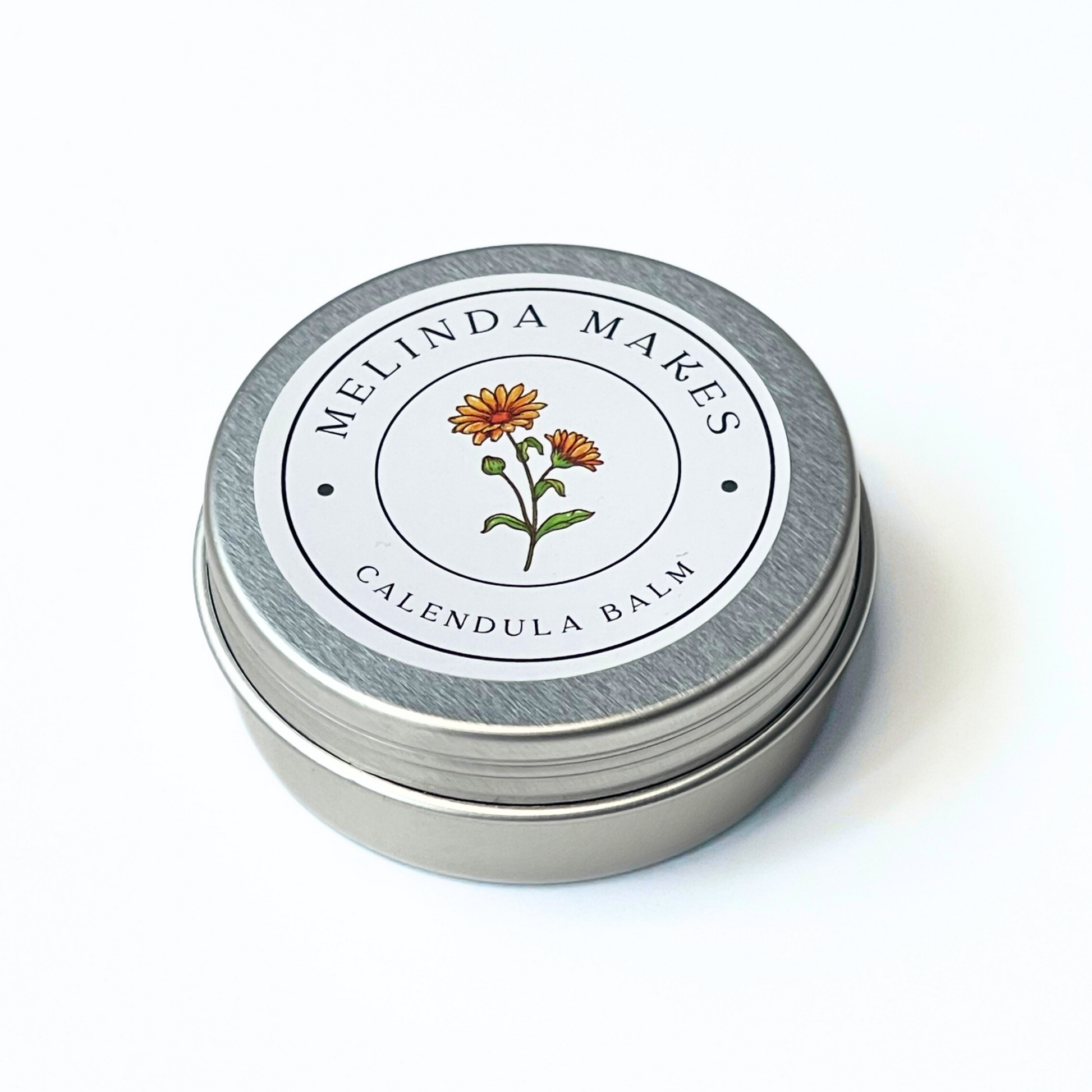 Metal tin with 'Melinda Makes' label featuring with calendula floral design on a white background