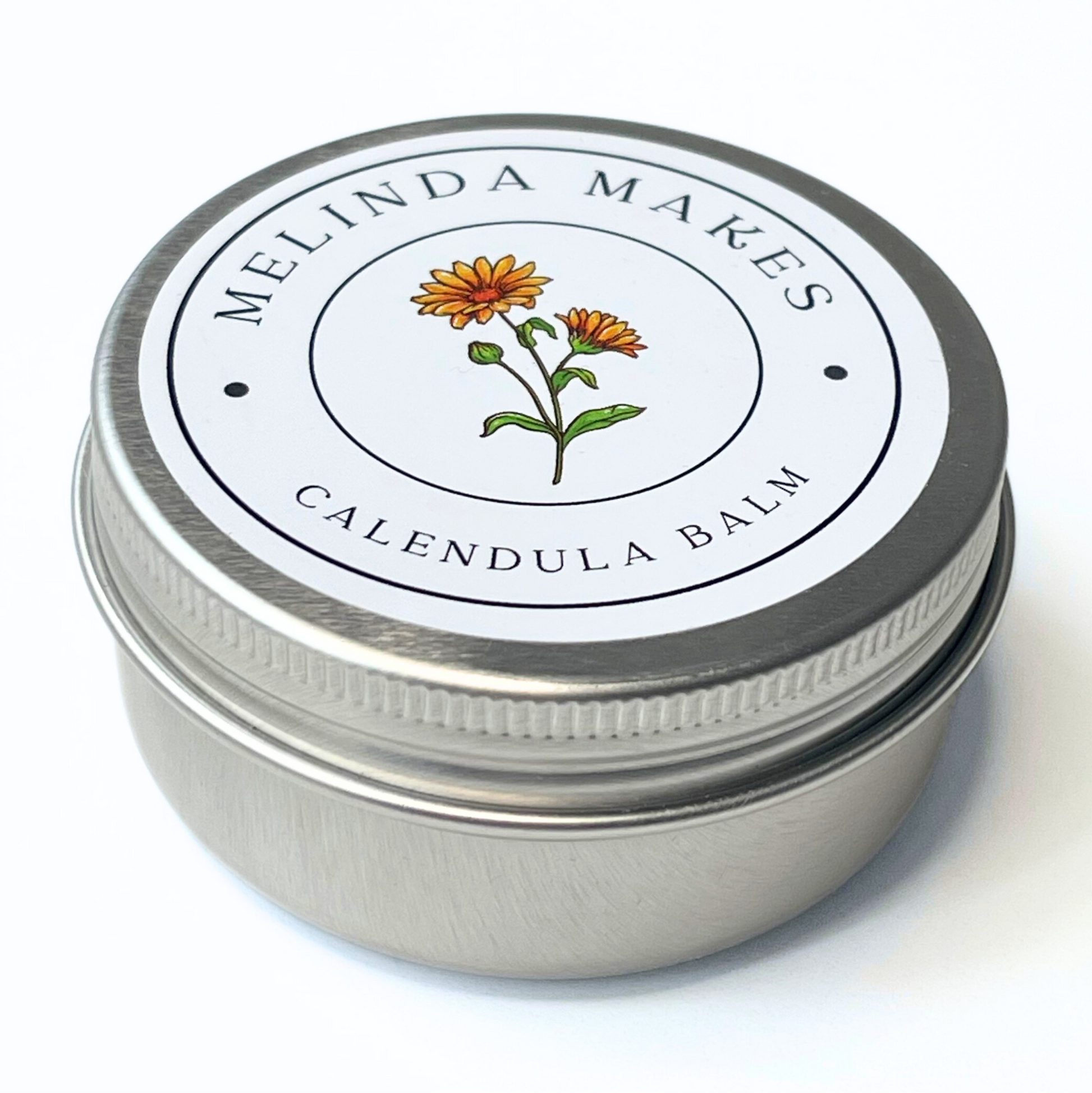 Metal tin with 'Melinda Makes' calendula balm with calendula floral on it on a white background