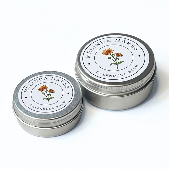 Both size tins of Melinda Makes Calendula Balm with calendula floral on it on a white background