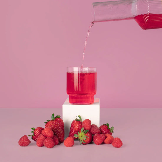  mixed berry hydramama being poured into glass with strawberry and raspberries sitting