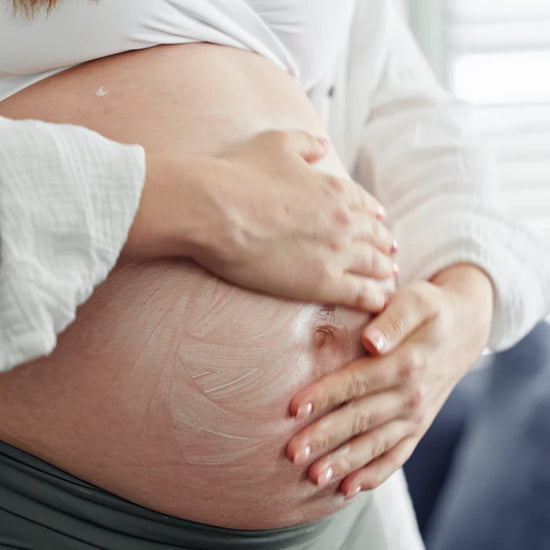 Close-up of a pregnant belly with hands gently cradling it rubbing in mumma's moisturiser
