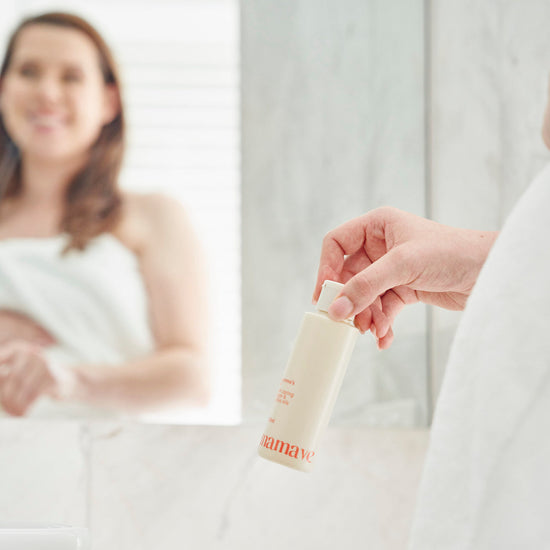 Person holding a bottle of Mamava Mumma's Pregnancy and Postpartum Oil in bathroom with towel product with a blurred background