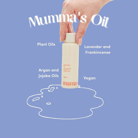 Hand holding a cap bottle of 'Mumma's Oil' against a blue background with product details plant oils, argan and jojoba oils, vegan, lavender and franincense. 