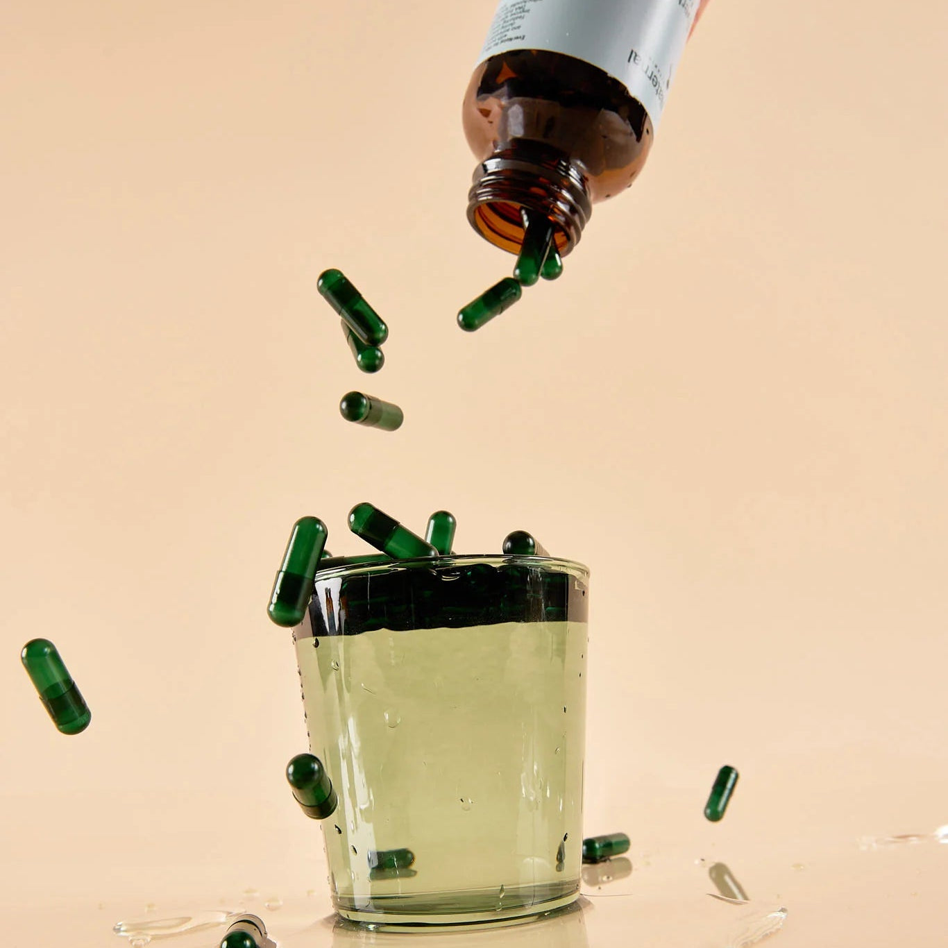 Hand pouring evernatal for him capsules into a glass of liquid on a beige background