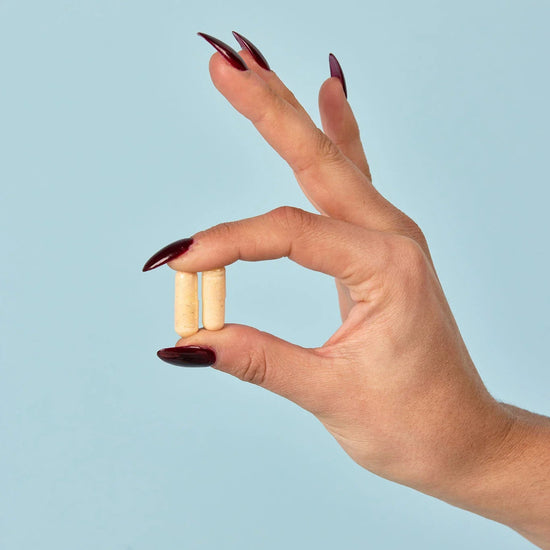 Hand holding two small cylindrical tablets against a light blue background