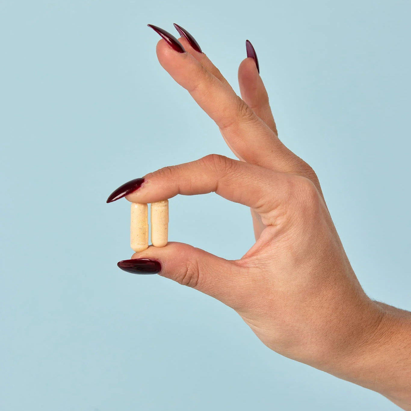 Hand holding two small cylindrical tablets against a light blue background