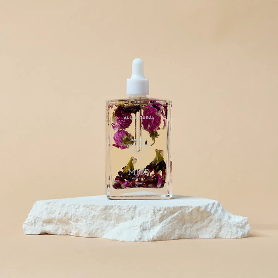 Bottle of floral oil with dried flowers on organic nourishing body oil a beige background with a stone