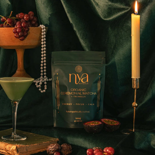 Nya Naturals matcha package with a cocktail, grapes, and candle on a dark background