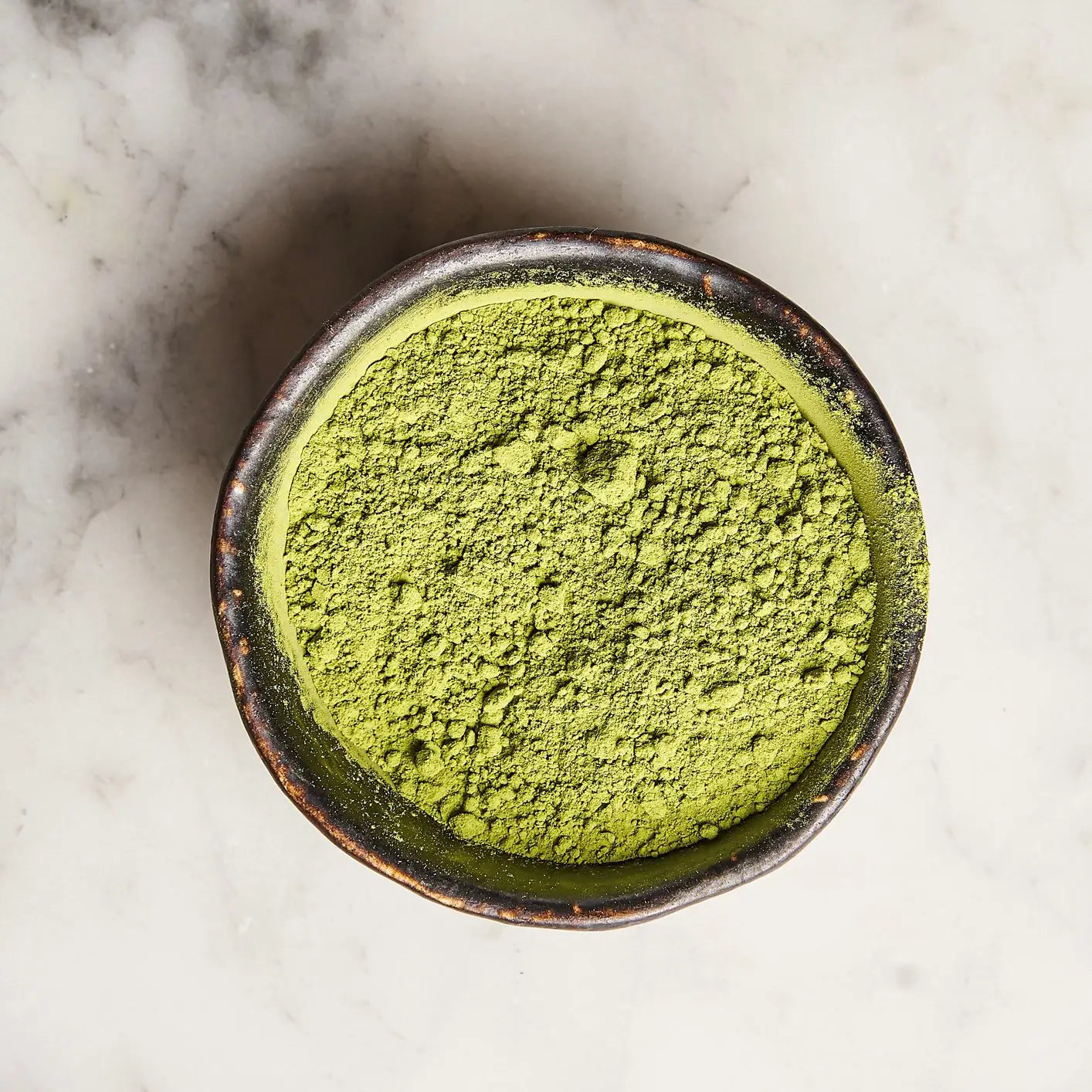 Bowl of green matcha powder on a marble surface