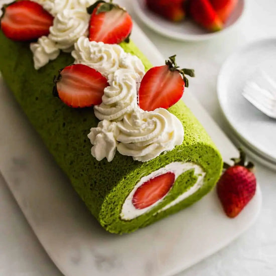 Green cake roll with strawberries and cream on a marble surface