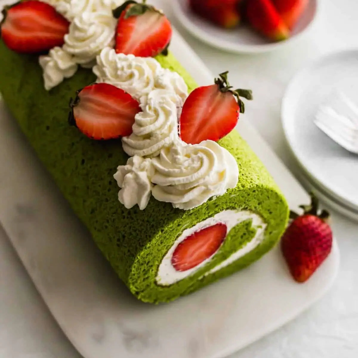 Green cake roll with strawberries and cream on a marble surface