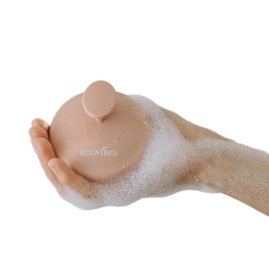 Hand holding a pink bath bomb labeled 'ECOVIBES' with bubbles on a light background