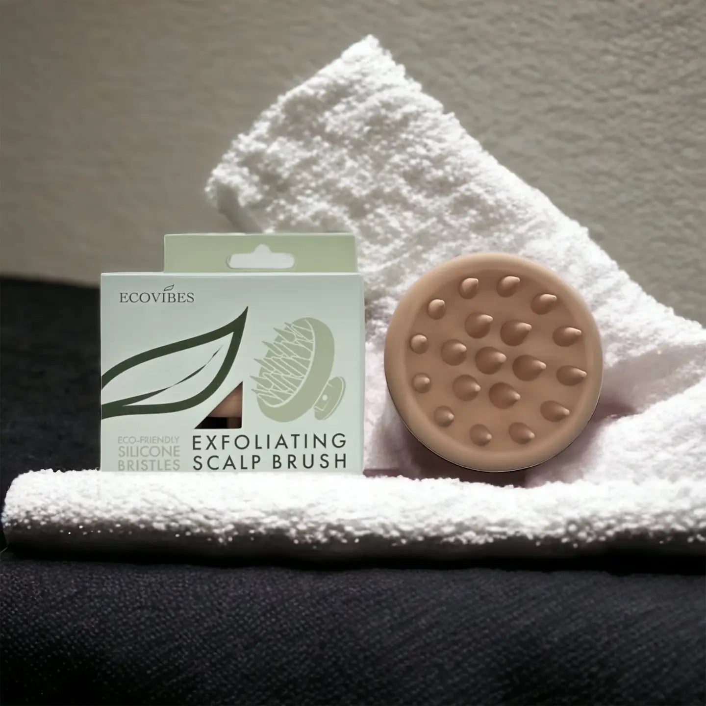 Exfoliating scalp brush with packaging on a white towel