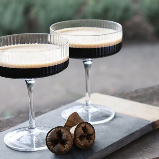Two espresso martinis in a ribbed glasses sitting on a stone cutting board