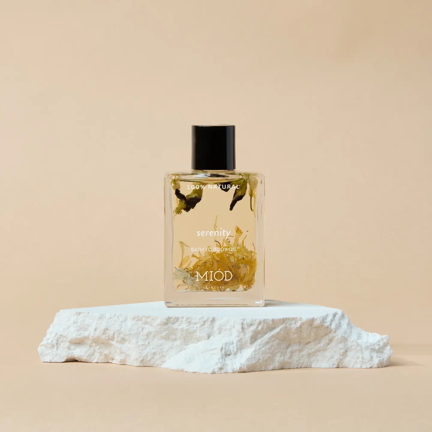 Serenity bath to body oil 100% natural miod glass bottle with black lid and flowers in it. On a rock background. 