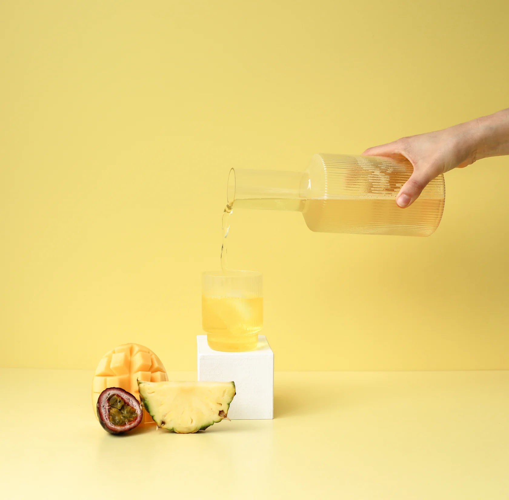 tropical hydramama being poured int glass with mango, passion fruit and pineapple sitting